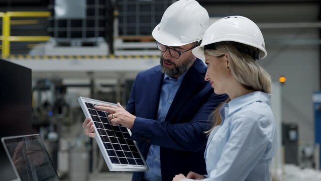 Female engineer and male director talking in modern industrial factory about solar panels installation, solar energy for company. Team management in manufacturing facility, green renewable energy for