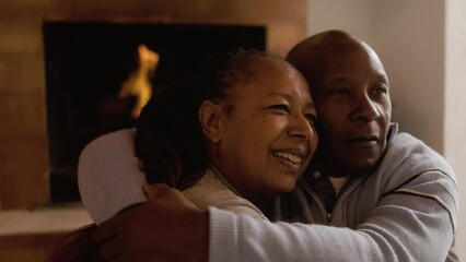 Senior couple by cozy fireplace having tender moment together. African american elderly people hugging in wood house - Powered by Adobe