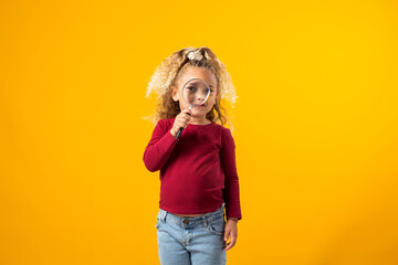 Litle girl holding a magnifier in hand, exploring the world with curiosity, wonder, and a keen sense of discovery. Education and curiosity concept