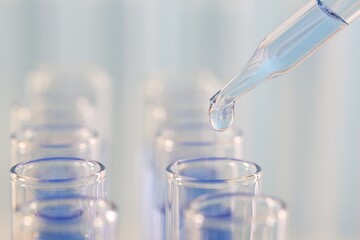 Laboratory analysis. Dripping light blue liquid from pipette into glass test tube on blurred background, closeup