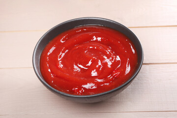 Delicious ketchup in bowl on light wooden table, closeup. Tomato sauce