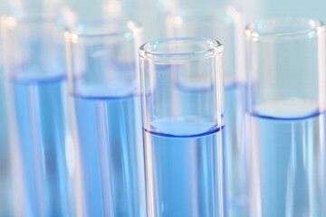 Laboratory analysis. Many glass test tubes with light blue liquid on blurred background, closeup