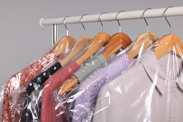 Dry-cleaning service. Many different clothes in plastic bags hanging on rack against grey...