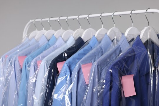 Dry-cleaning service. Many different clothes in plastic bags hanging on rack against grey background
