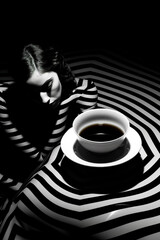 black and white studio shot of woman lying and drinking coffee, stylish striped dark shot with shadows, female drink espresso