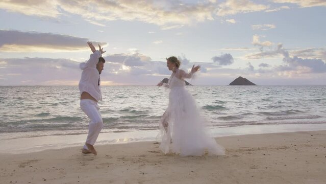 Expressive man and woman in wedding dress performing hilarious weird voodoo dance on sandy beach at sunrise. Funny passionate people making comic mating dance moves.Couple in love happy on wedding day