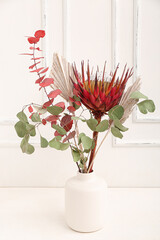 Vase with beautiful protea flower on table in room
