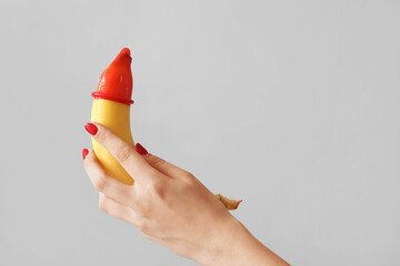 Woman holding banana with condom on light background. Sex concept - obrazy, fototapety, plakaty