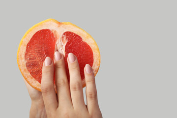 Woman with half of grapefruit on light background, closeup. Sex concept - obrazy, fototapety, plakaty