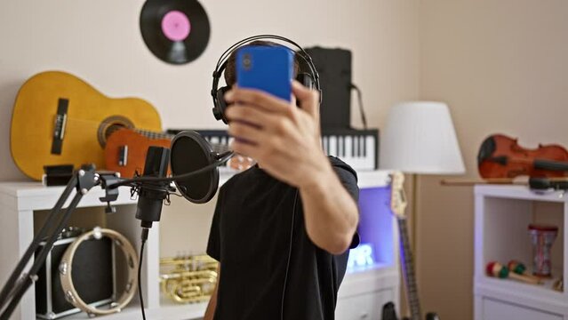 Attractive young hispanic man, a professional musician, smiling while making a self-portrait with his smartphone in a music studio