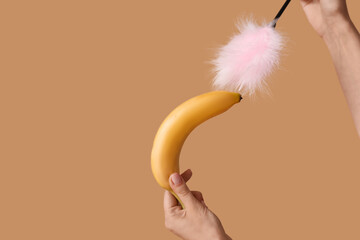 Young woman with banana and feather stick on beige background. Sex concept