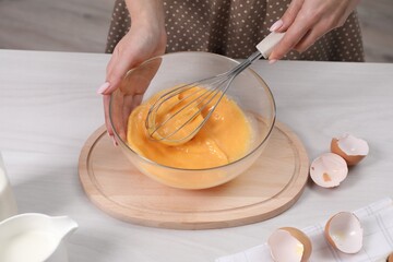 Woman whisking eggs in bowl at table indoors, closeup