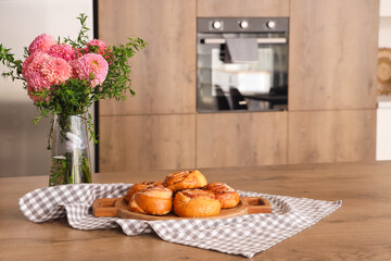 Vase with flowers and buns on table in kitchen