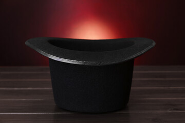 Black magician top hat on wooden table against color background, closeup