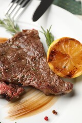 Delicious grilled beef steak with spices and lemon on plate, closeup