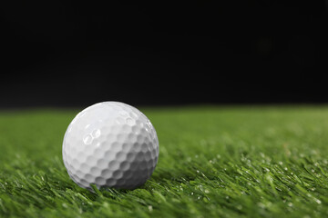Golf ball on green grass against black background, space for text