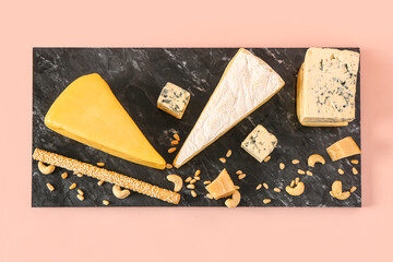 Board with tasty cheese, nuts and grissini on pink background