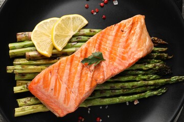 Tasty grilled salmon with asparagus, lemon and spices on black plate, top view