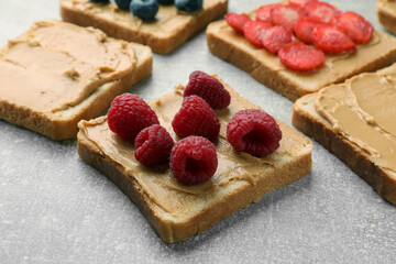 Tasty peanut butter sandwiches with fresh berries on gray table, closeup