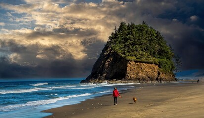 A woman in a red sweatshirt walking a golden retreiver on the beach with Proposal rock in...