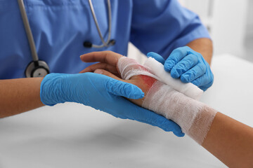 Doctor bandaging patient's burned hand at table, closeup