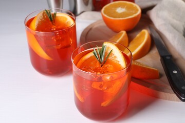 Aperol spritz cocktail, rosemary and orange slices on white table, closeup