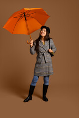 Beautiful young Asian woman with umbrella on brown background
