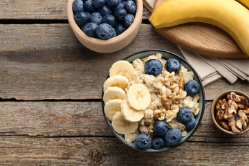 Tasty oatmeal with banana, blueberries and walnuts served in bowl on wooden table, flat lay. Space for text