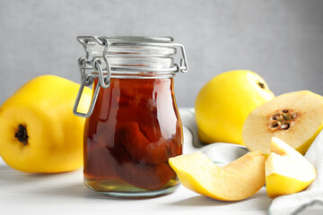 Tasty homemade quince jam in jar and fruits on white wooden table, closeup