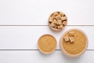 Obraz na płótnie Canvas Different types of brown sugar in bowls on white wooden table, flat lay. Space for text