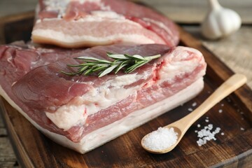 Pieces of raw pork belly, salt and rosemary on wooden table, closeup