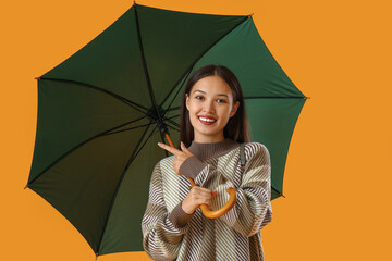 Beautiful young Asian woman pointing at umbrella on yellow background