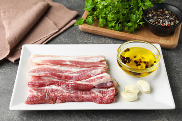 Pieces of raw pork belly, oil, parsley and garlic on grey textured table