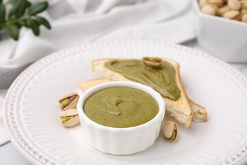 Tasty pistachio cream in bowl, nuts and toasts on table, closeup