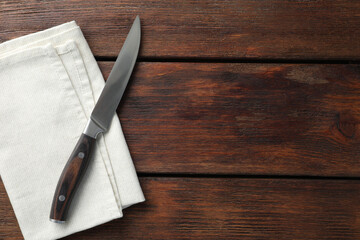 One sharp knife and napkin on wooden table, top view. Space for text