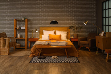 Interior of bedroom with armchairs, glowing lamps and wooden bench at night