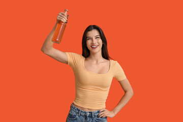 Beautiful young woman with bottle of cold beer on orange background