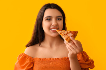 Young woman eating piece of tasty pizza on yellow background