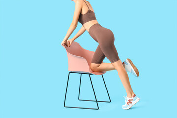 Young woman in cycling shorts with chair on blue background
