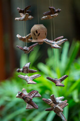 Birds made with clay and painted for a hanging by a potter in front of a lush green foliage