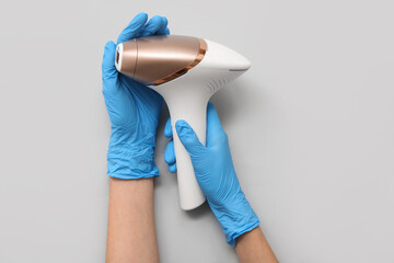 Female hands in rubber gloves with modern photoepilator on grey background, closeup