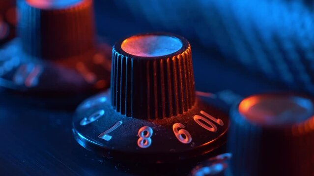 Adjusting a dusty old volume knob on a electric guitar amplifier. 80's nostalgia teal and orange lighting. Carbon fiber textured amp
