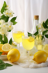 Limoncello liquor in two glasses with lemons and flowers on the light background