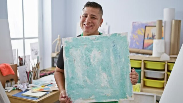 Confident young latin man smiling joyously, proudly displaying his flair in drawing at art studio, exuding creativity and passion.
