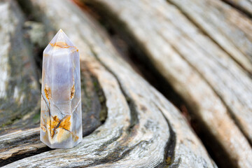 A close up image of a blue lace healing crystal tower standing on a faded and cracked driftwood...