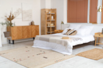 Blurred view of stylish bedroom with paintings, commode and shelf unit