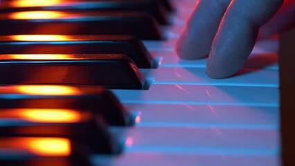 A musician's finger gracefully presses against the neon illuminated keys of a piano, casting a warm orange and cool blue glow that dances across this intimate portrayal of artistic expression and the 