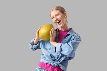 Young woman with pomelo on light grey background
