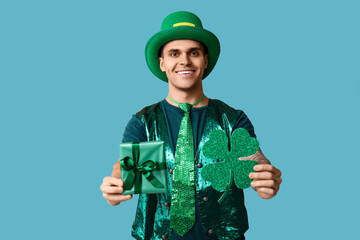 Happy young man in green clothes, with gift and shamrock on blue background. St. Patrick's Day