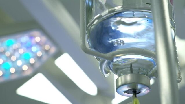  glass bottle with saline solution or medicine hanging on medical IV  close-up . Bright operating room in modern medical facility or clinic.
